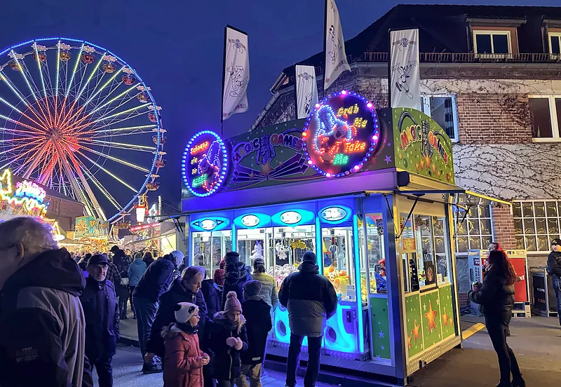 Der kleine Greifer abends vor einem Riesenrad, umringt von Besuchern.