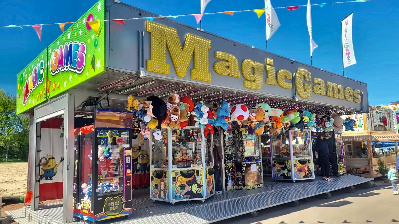 Magic Games im Sommer: goldener Leuchtschriftzug über einer offenen Front voller Spielgeräte und Gewinne.